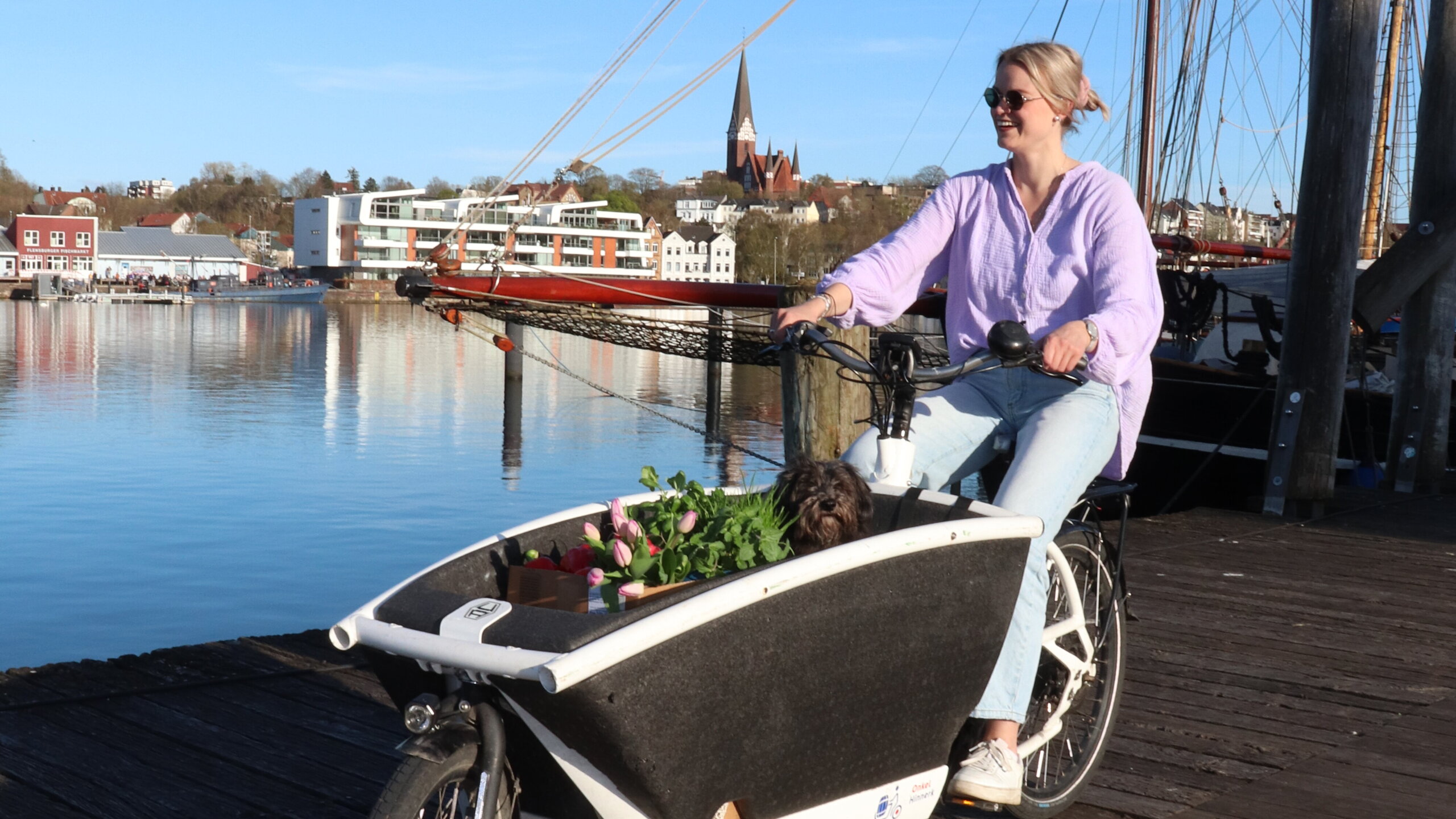 Eine Frau fährt mit einem Lastenfahrrad am Wasser entlang