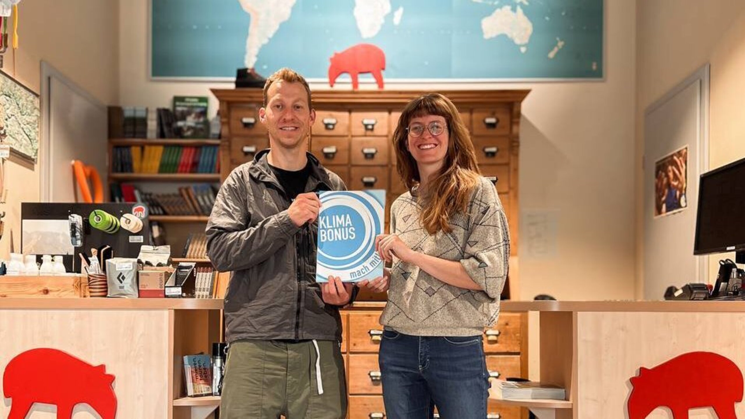 2 Personen stehen in einem Laden und halten ein Klimabonus-Schild in die Kamera